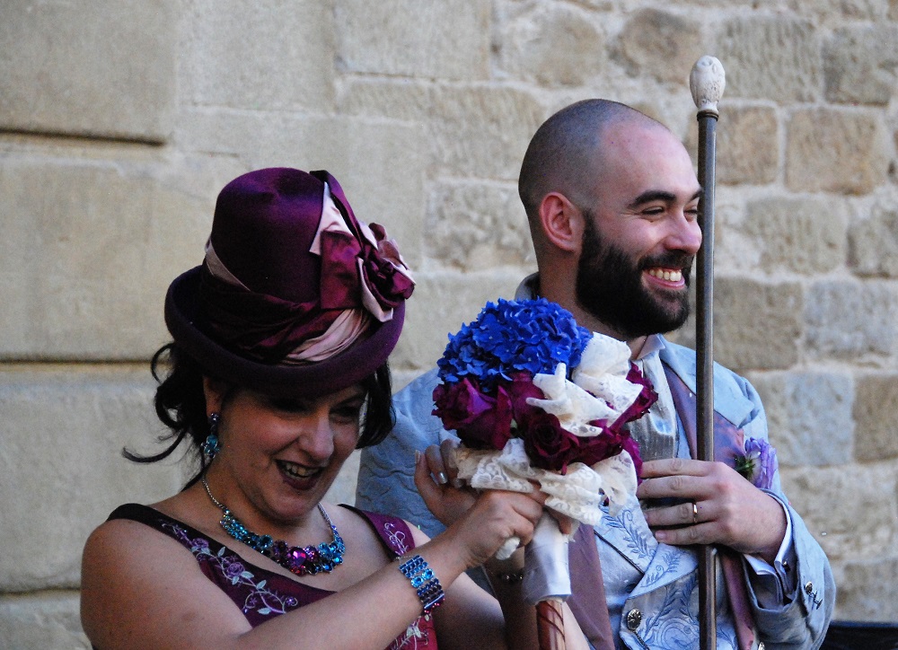 Happy Spouses wearing top hats, with a bouquet on a stick and a walking stick.