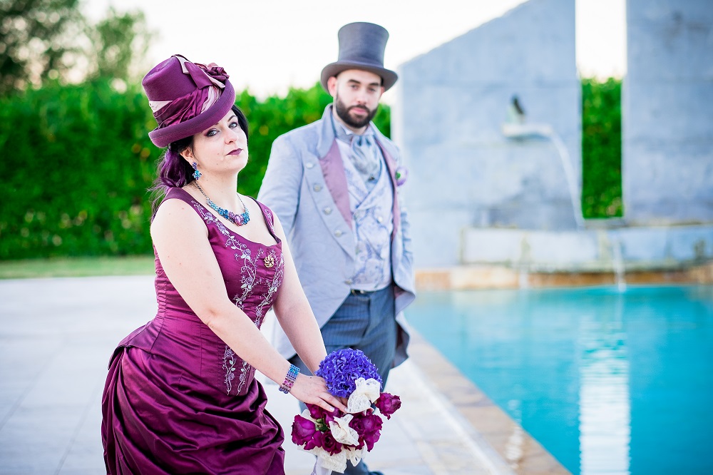 Spouses dressed in late victorian era fashion, in front of a monument