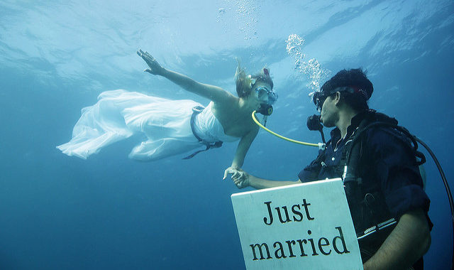 Foto di due sposi sott'acqua, lo sposo ha un cartello 