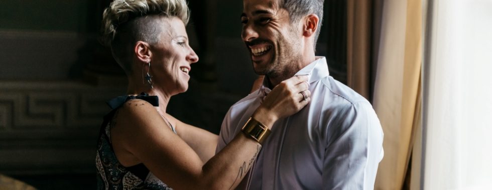 The sister of the groom helps him getting dress with his suit